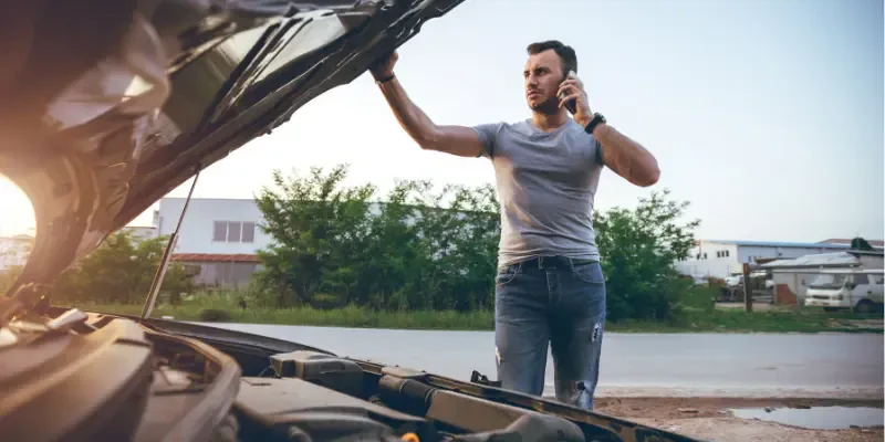 homem no celular falando com a assistência técnica ao lado de um carro com defeito