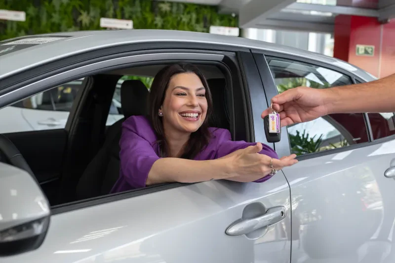 mulher de casaco roxo recebendo as chaves de um corolla sedan do godrive